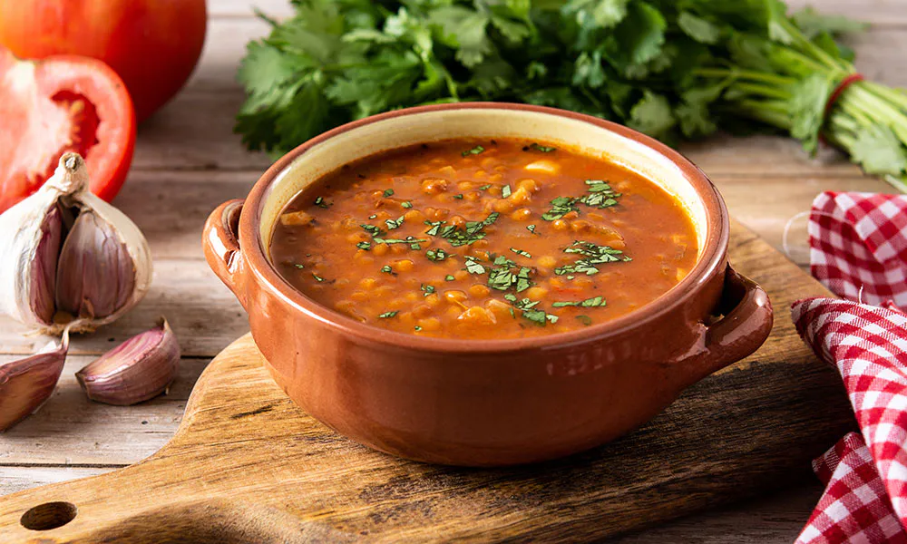 Hearty lentil tomato soup garnished with fresh cilantro in a terracotta bowl at Lahana Indian Cuisine, a Authentic Indian Cuisine Restaurant in New York